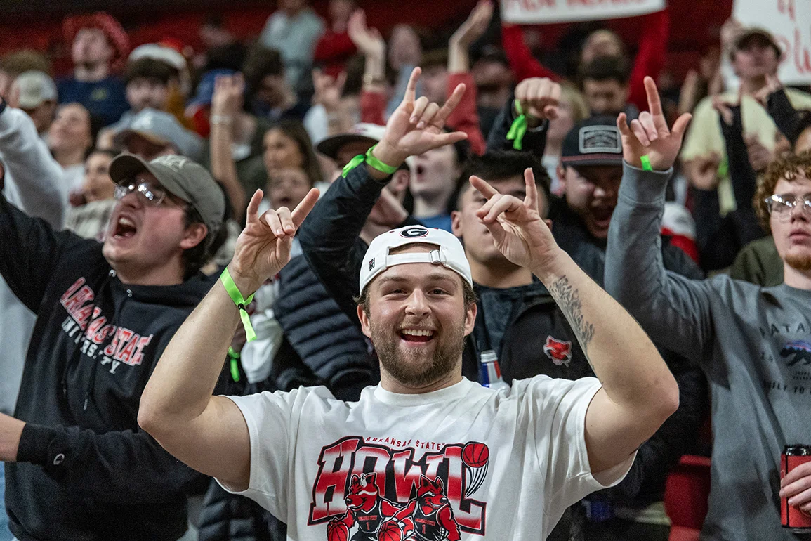 Students cheering and holding up Wolves Up at a basketball game.
