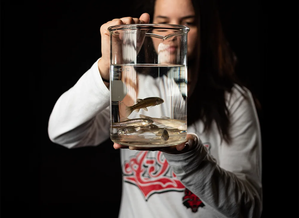 A-State student holding a beaker of live fish in water.