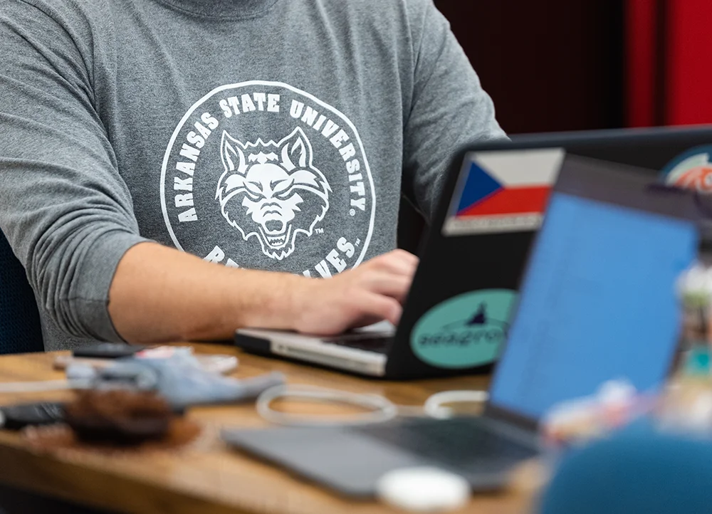 Close-up of student using a laptop in an A-State shirt