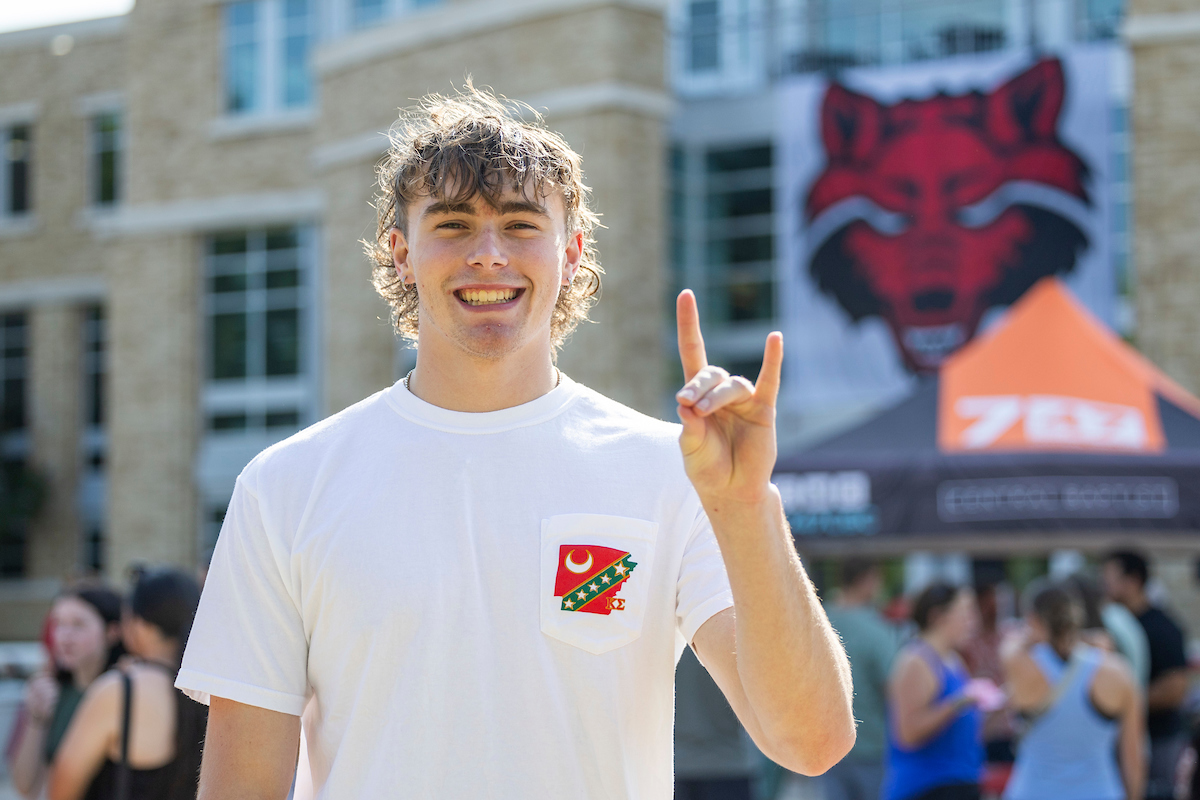 A smiling student puts their Wolves Up in front of the Reng Student Union