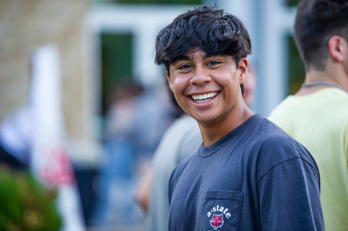 A-State student smiles while wearing a Red Wolves shirt at a campus event.