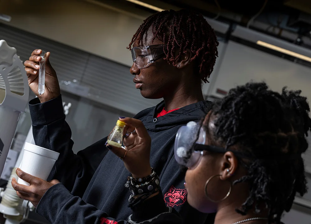 Two students in Red Wolves gear doing a chemistry experiment.