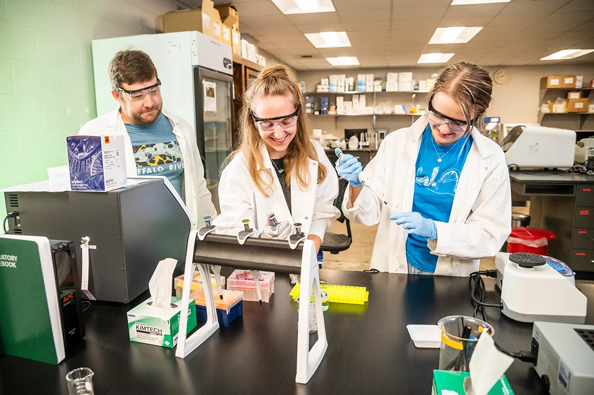 Two students and a professor smiling as they do a lab experiment.