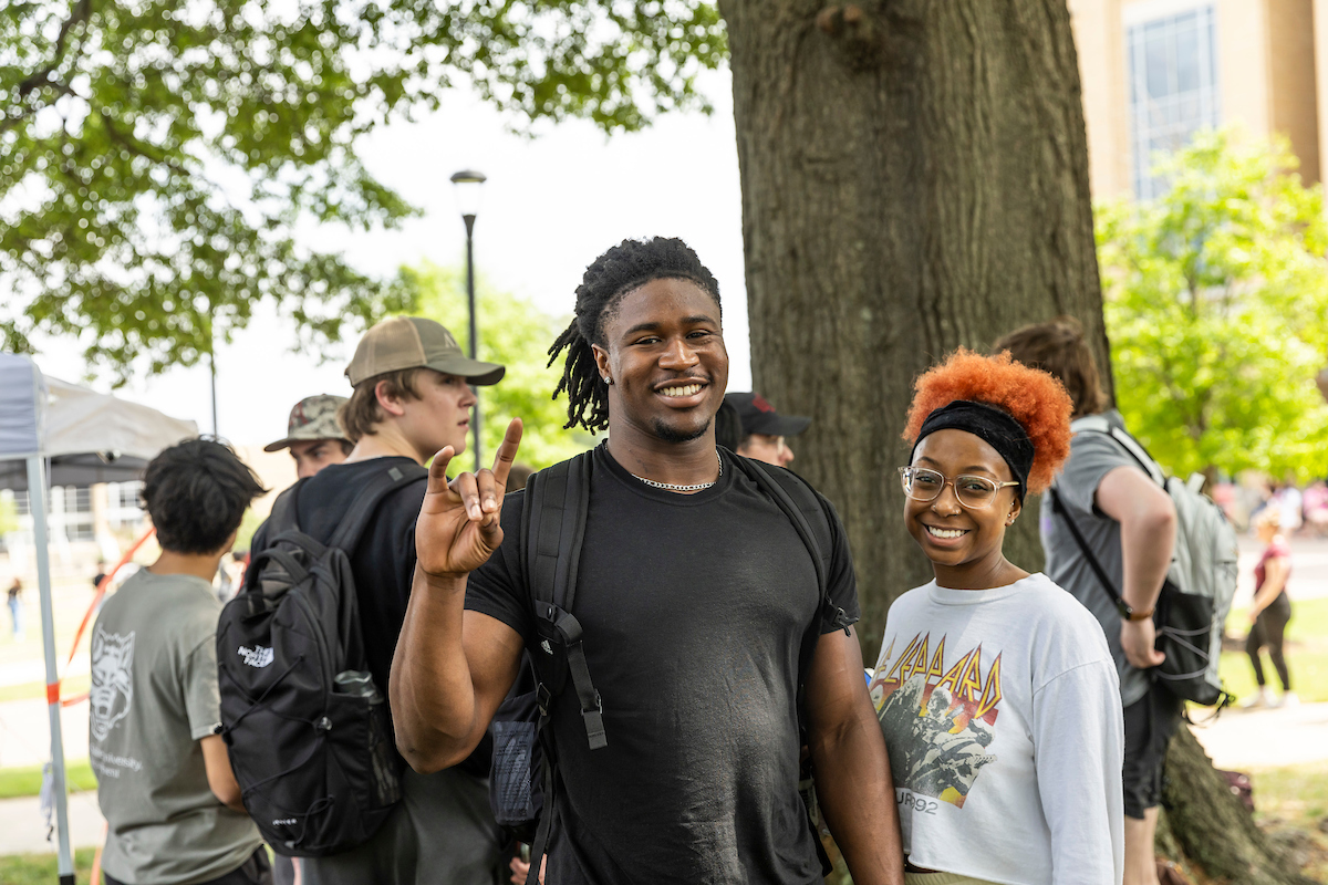 Two AState students smile during a campus event, with one showing their “Wolves Up!” hand sign. 