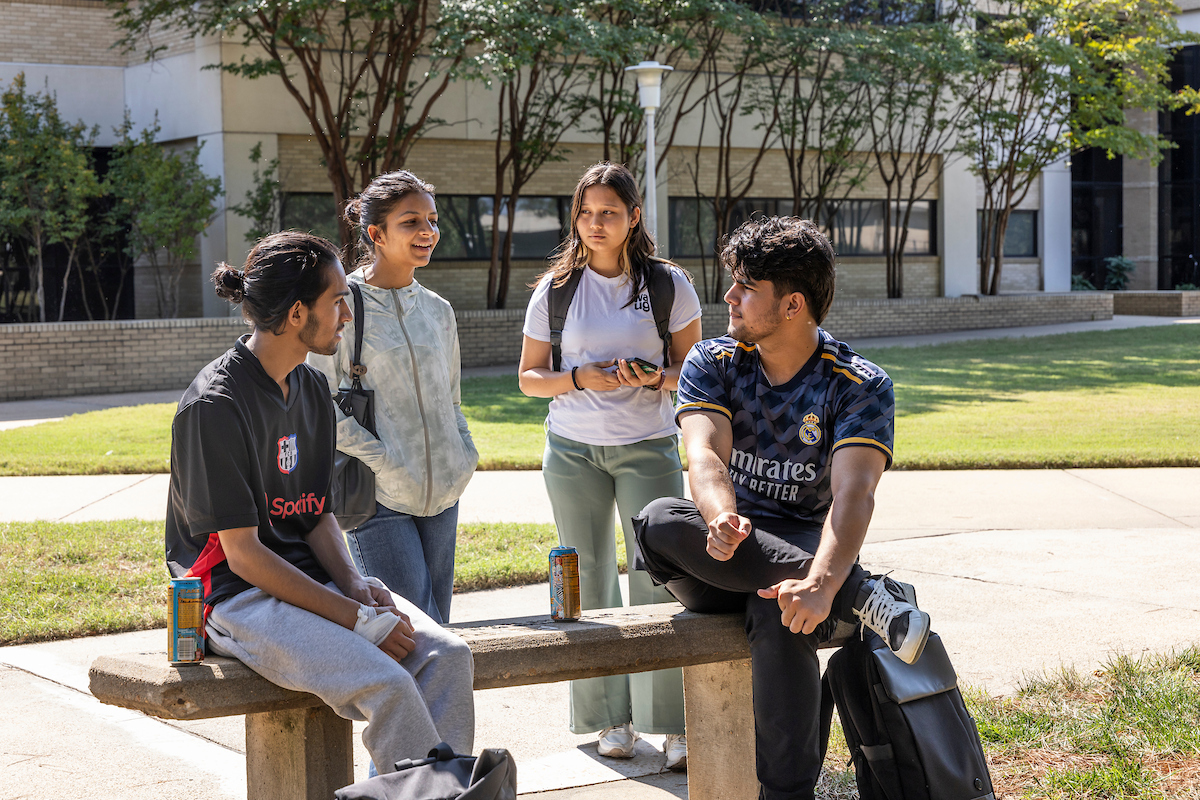 A-State students outside on a bench in the sun socializing.