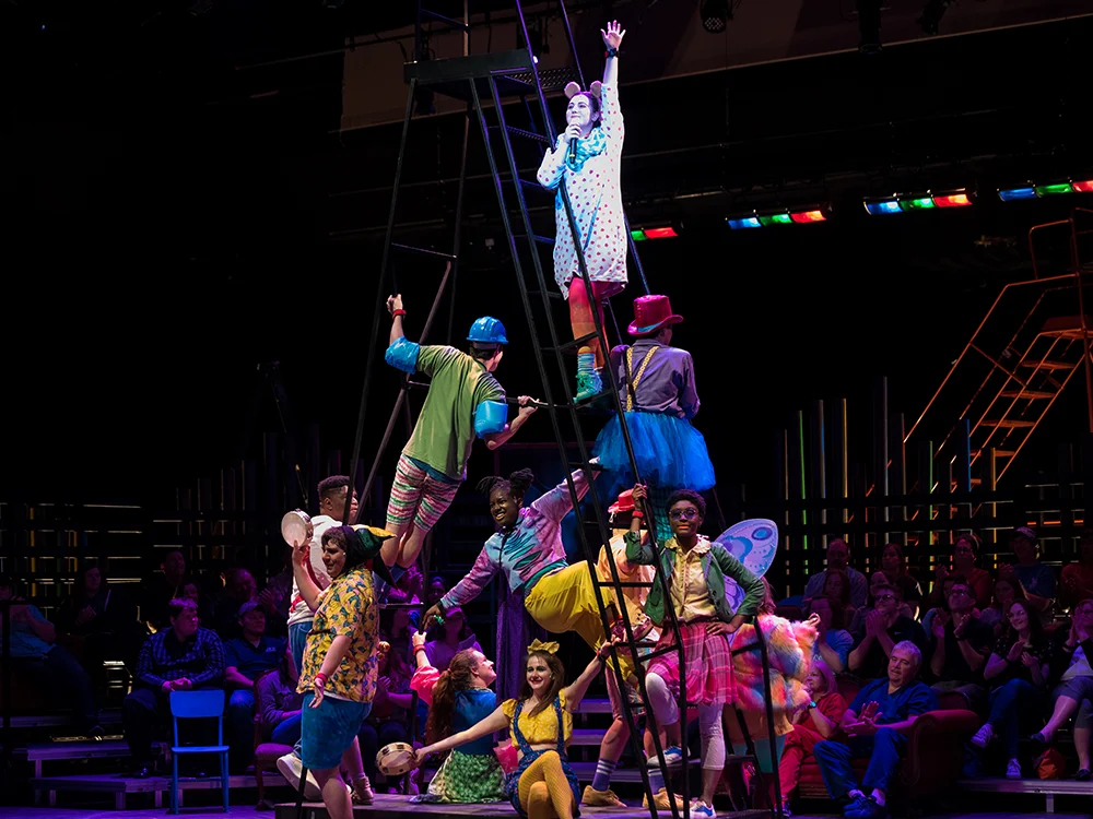 Actors in various costumes pose on a ladder.