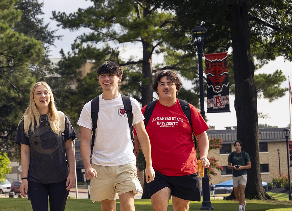 Three students smiling as they walk on campus.