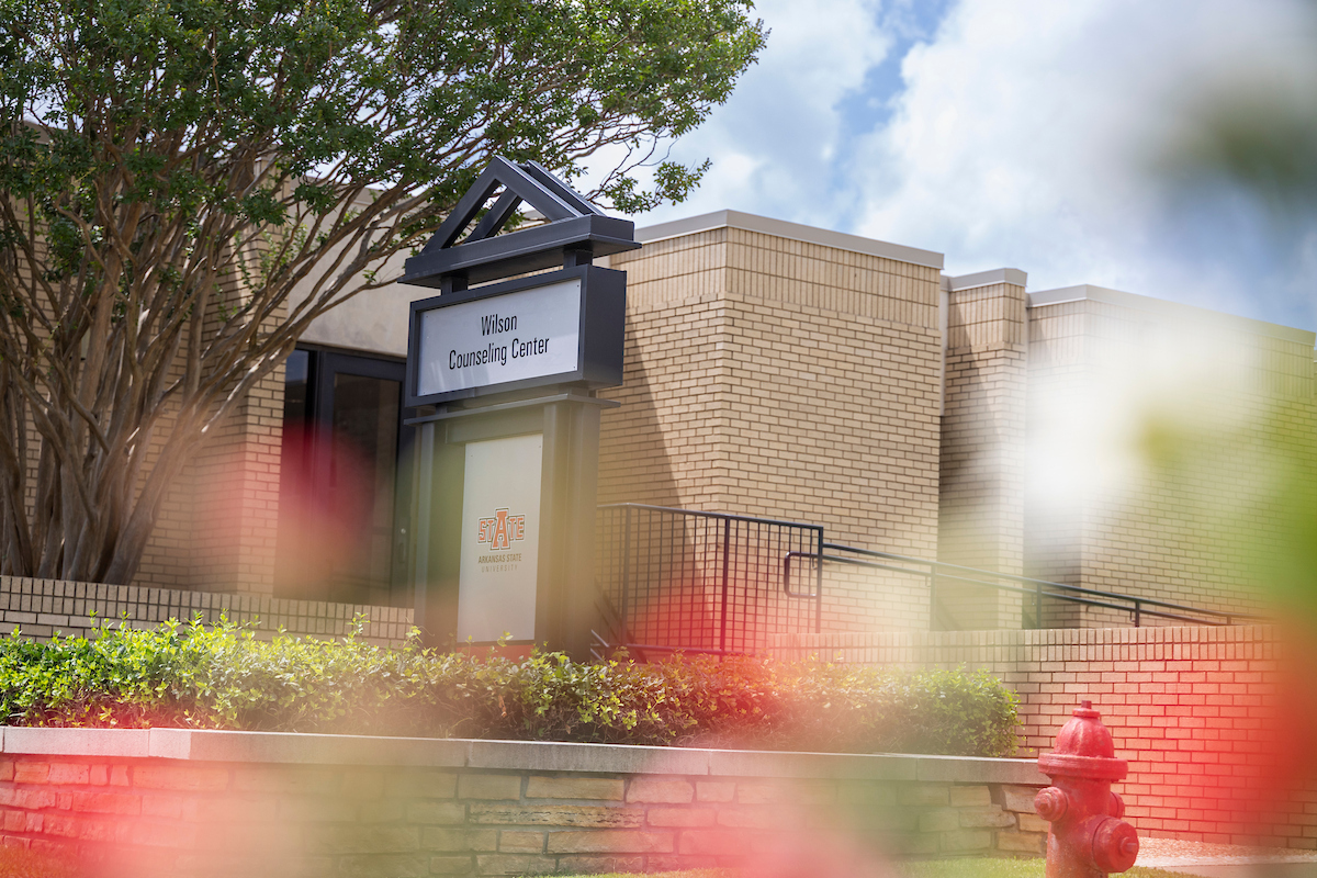 Wilson Counseling Center exterior with A-State sign, trees, flowers, and shrubs.