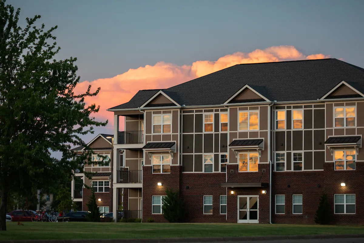 Brick and panel-style campus housing building glows in the reflection of a colorful sunset sky.