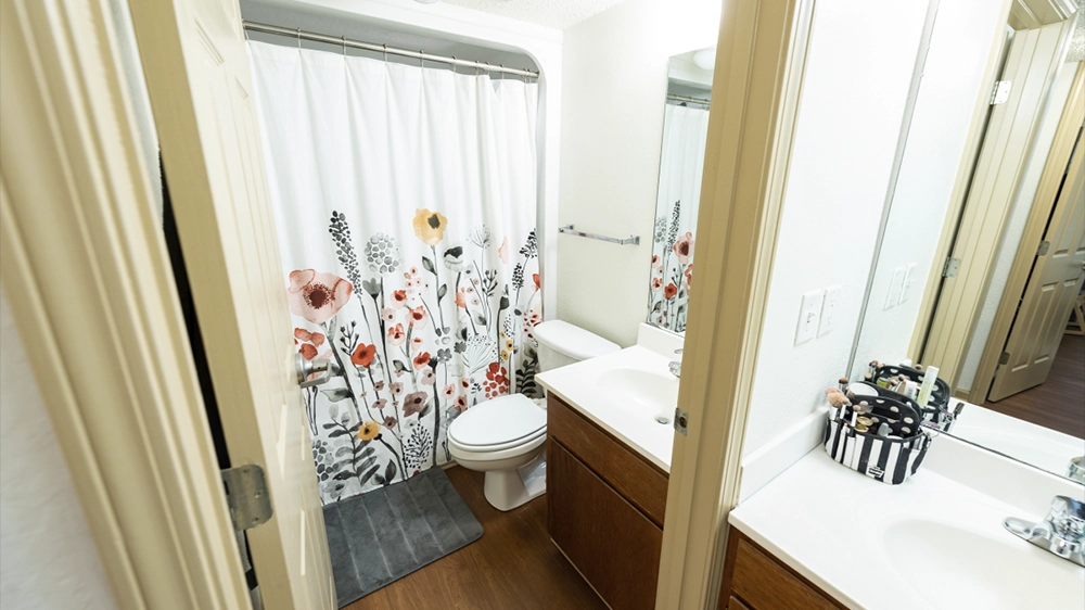 Close-up of a bathroom featuring a floral shower curtain, single sink vanity, and bright lighting.