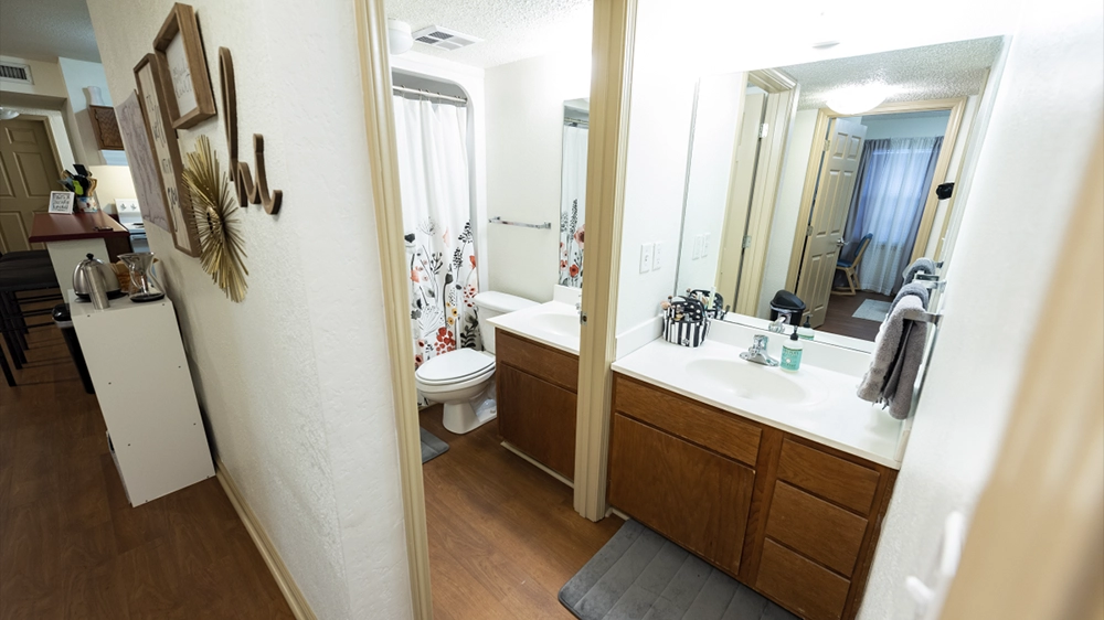 A bathroom with a double-sink vanity, large mirror, and a shower with a floral-patterned curtain. Neutral tones create a clean look.