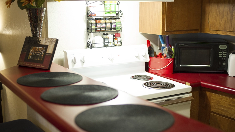 A kitchen with a white stove, microwave, and spice rack. A red countertop with black placemats adds a pop of color.