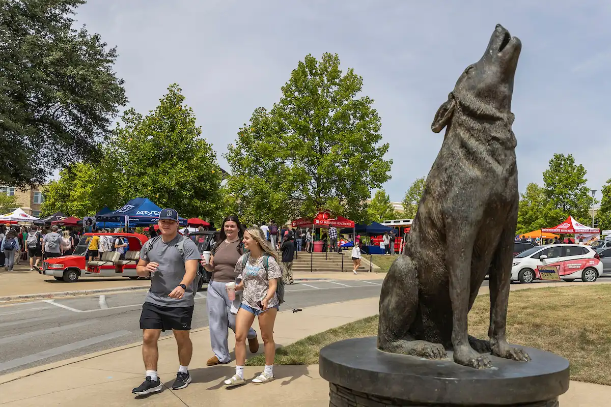 Students walking past wolf statue and tents at Community Fair event outside the Reng Student Union.