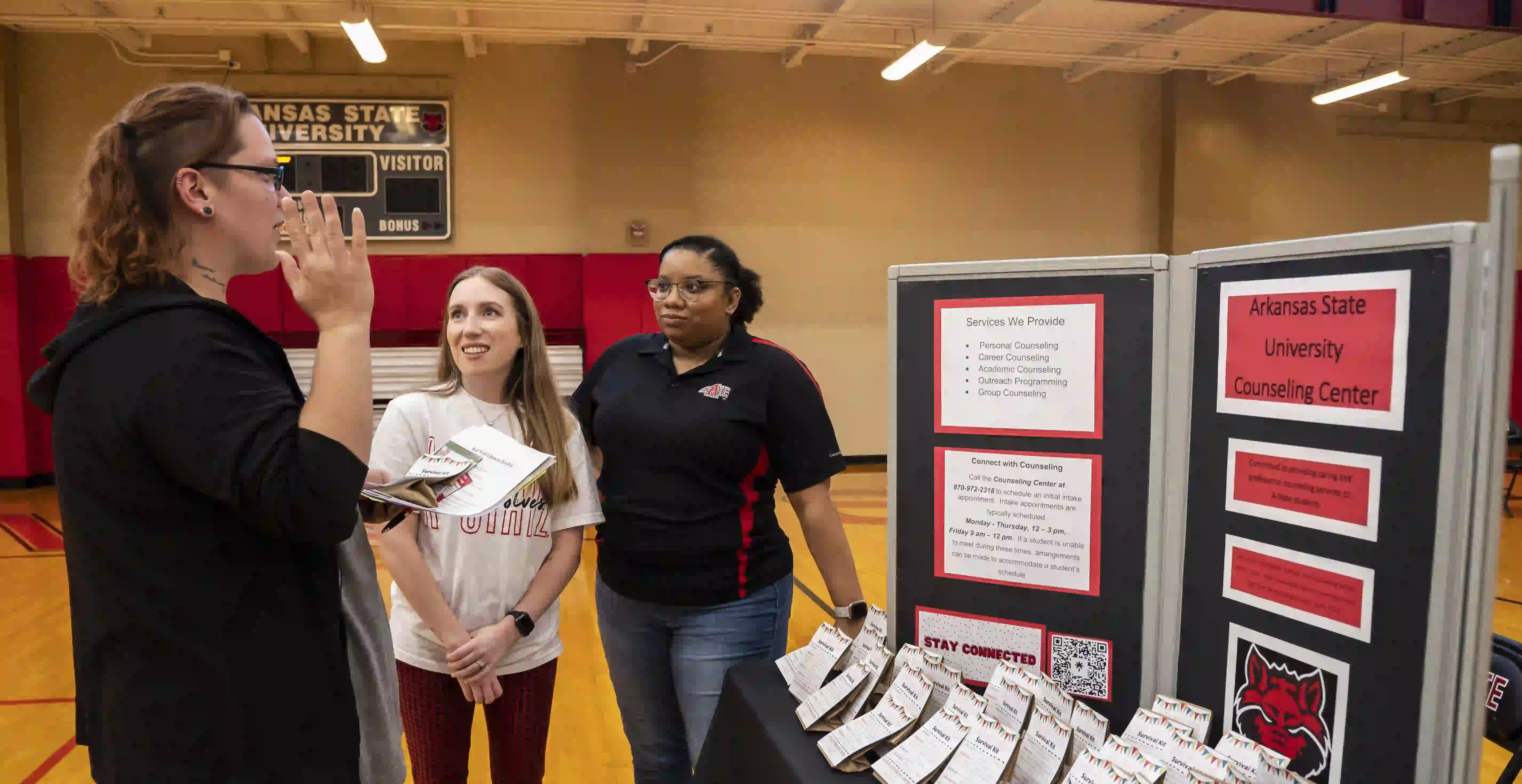 Counseling Center staff tabling and talking with student in gymnasium.