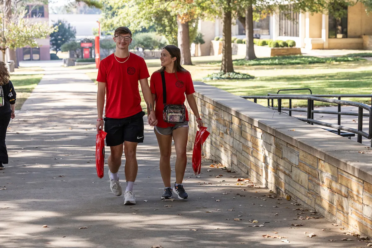 A boyfriend and girlfriend hold hands during a walking tour of campus.