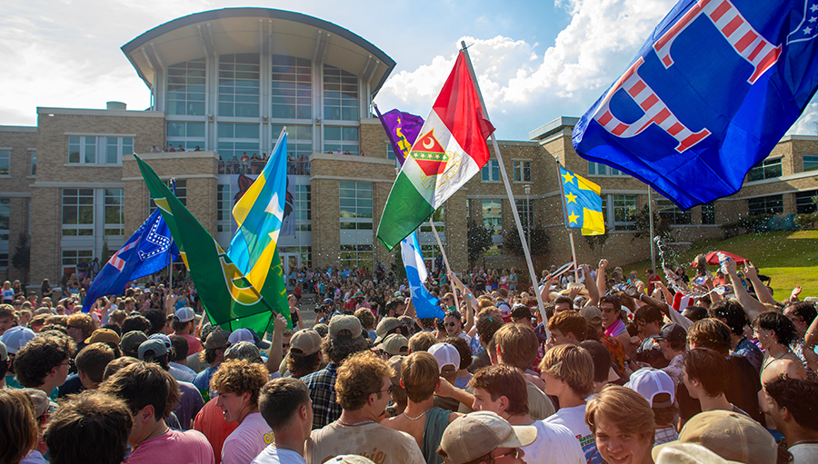 Fraternity flags fly above a crowd in front of the Reng Student Union at Fraternity Bid Day celebration.