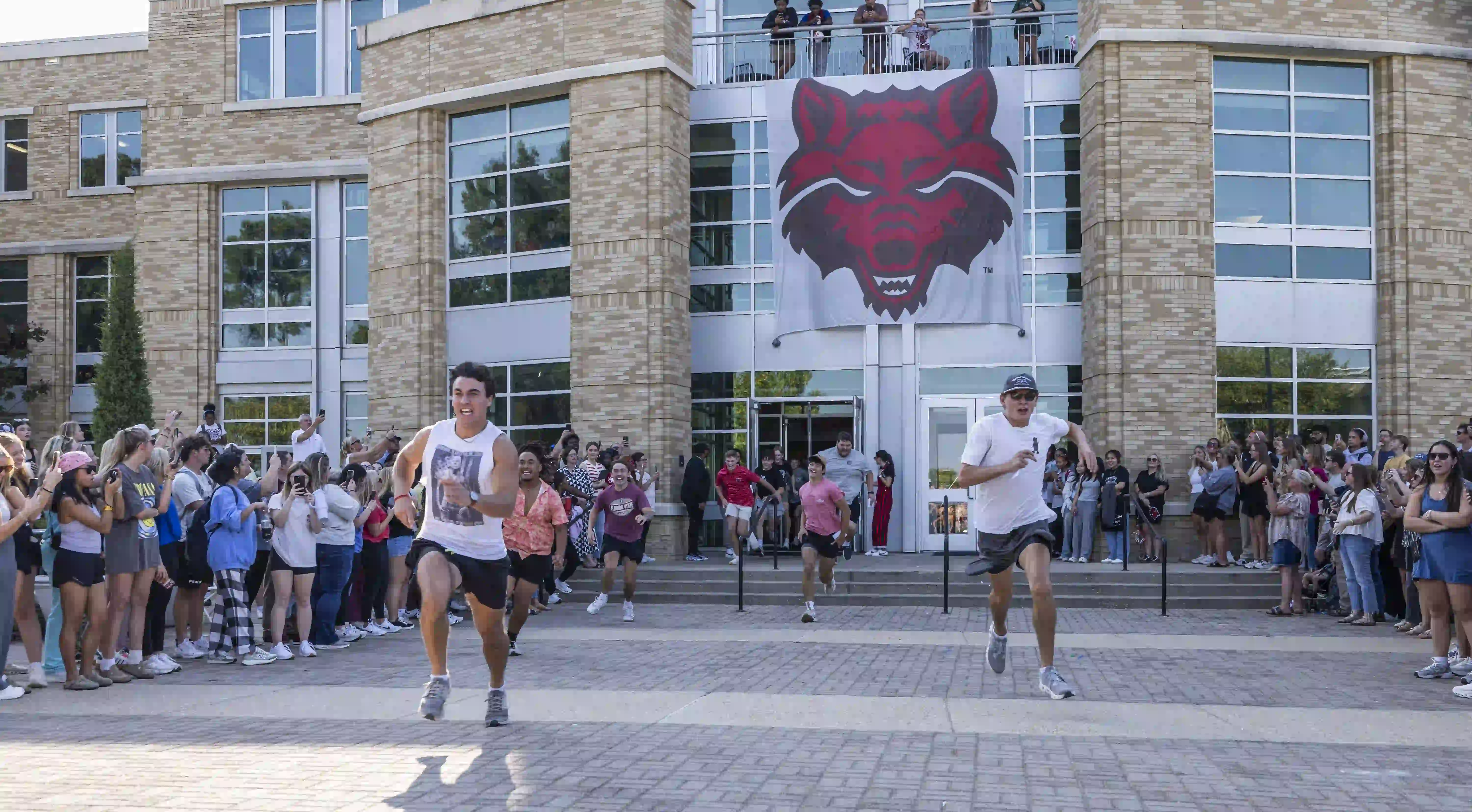 Men running in front of the Reng Student Union during Fraternity Bid Day celebration.