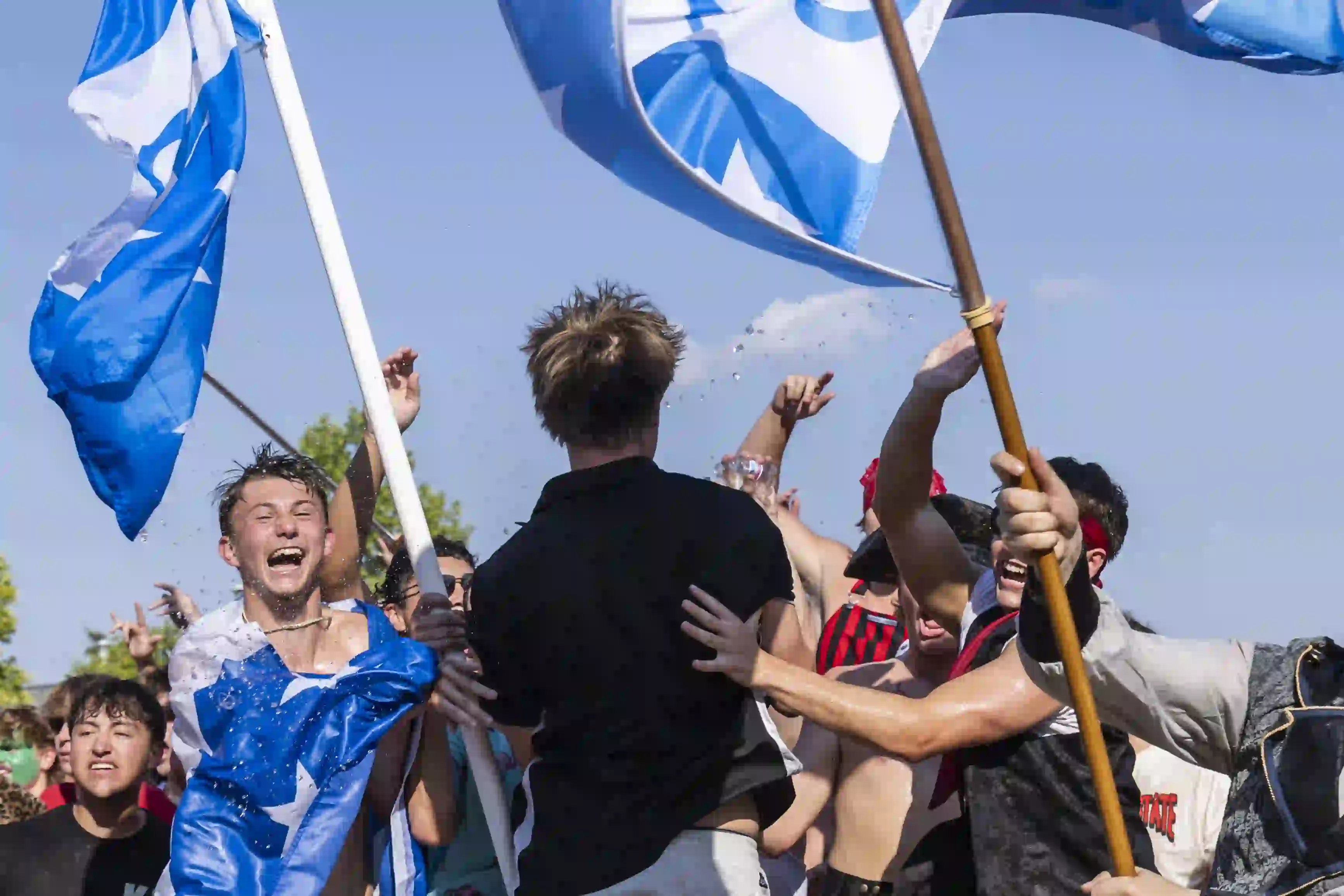 Men jumping and cheering with flags at Fraternity Bid Day celebration.