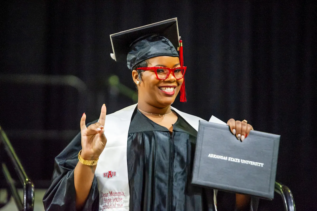 Grad giving a Wolves Up with her diploma.