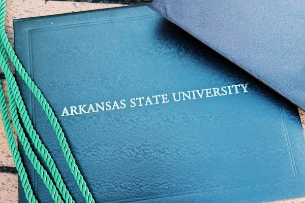 A green graduation cord rests beside a diploma cover embossed with “Arkansas State University,” symbolizing academic achievement and celebration.