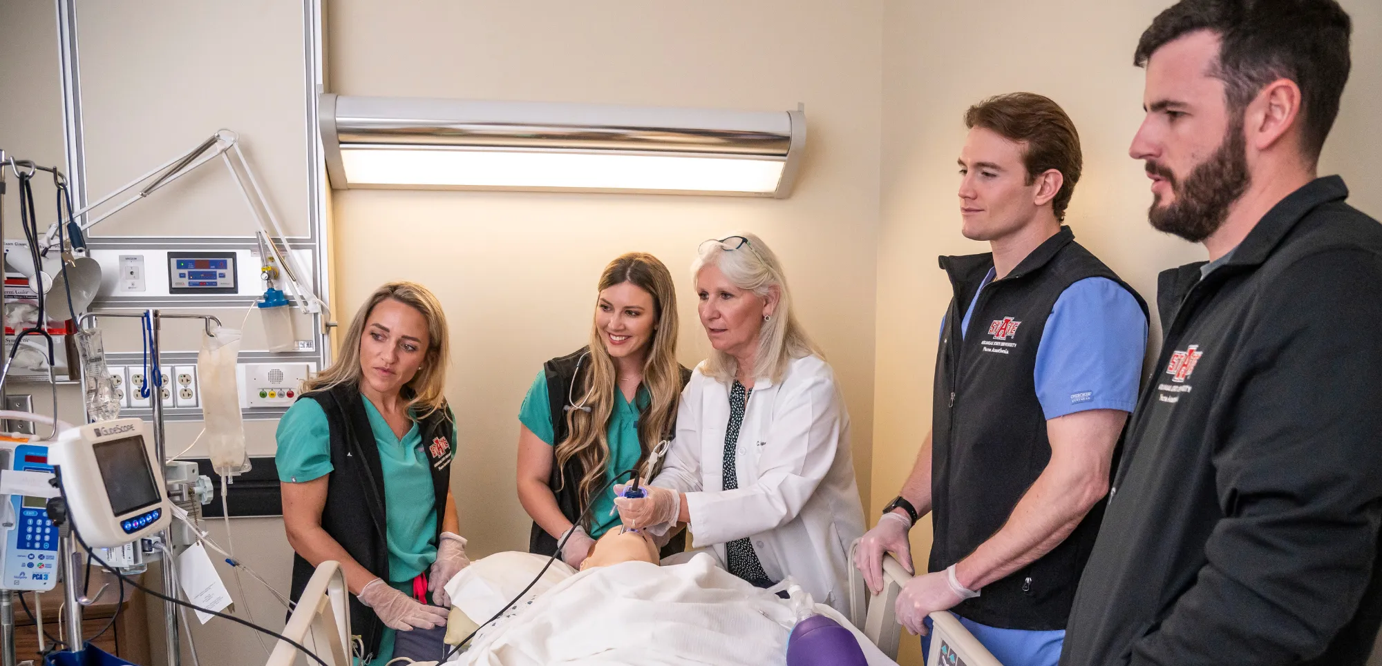 Nurse Anesthesia students gathered around the professor and a dummy on a hospital bed.