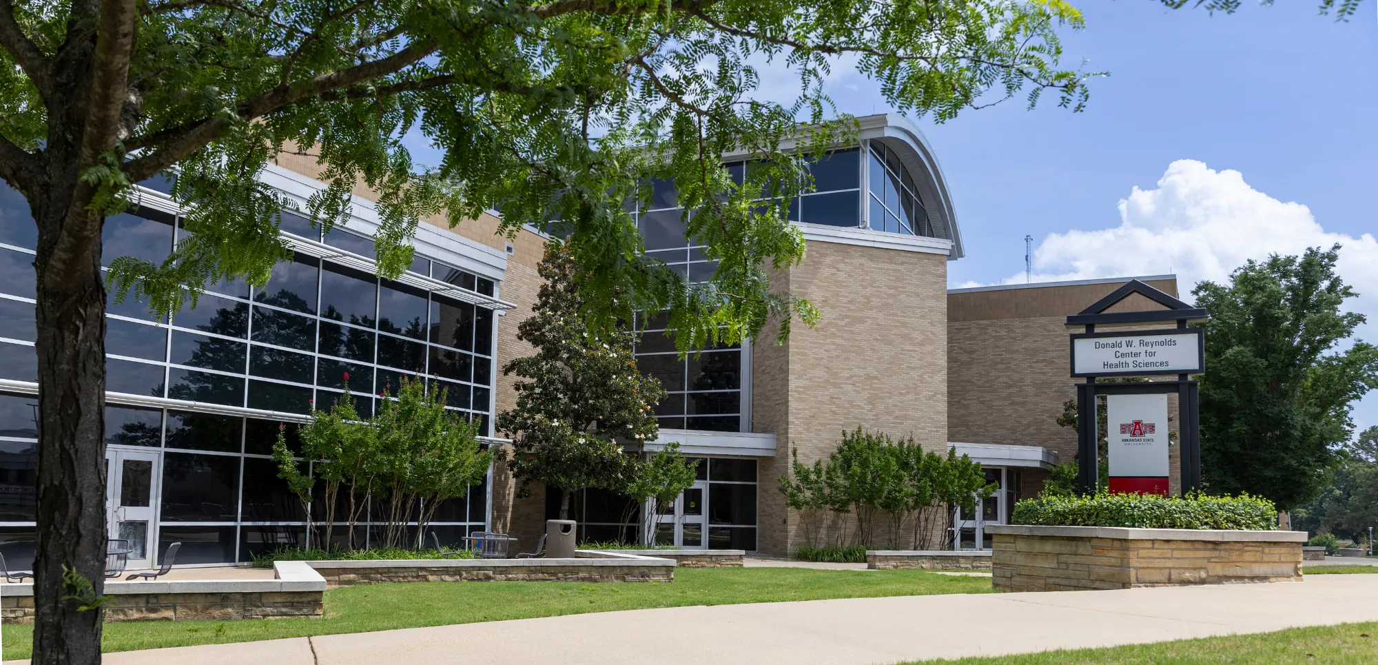 Donald Reynolds center for health sciences outside with a tree and sign in foreground.