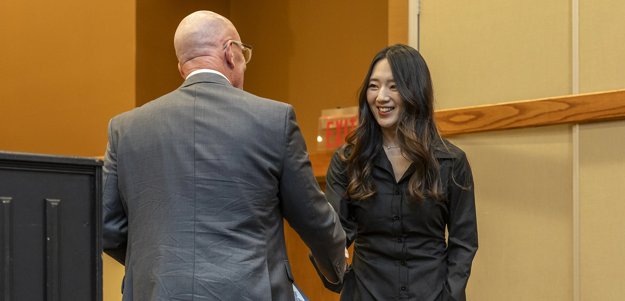 A student and professor shaking hands in formal attire.