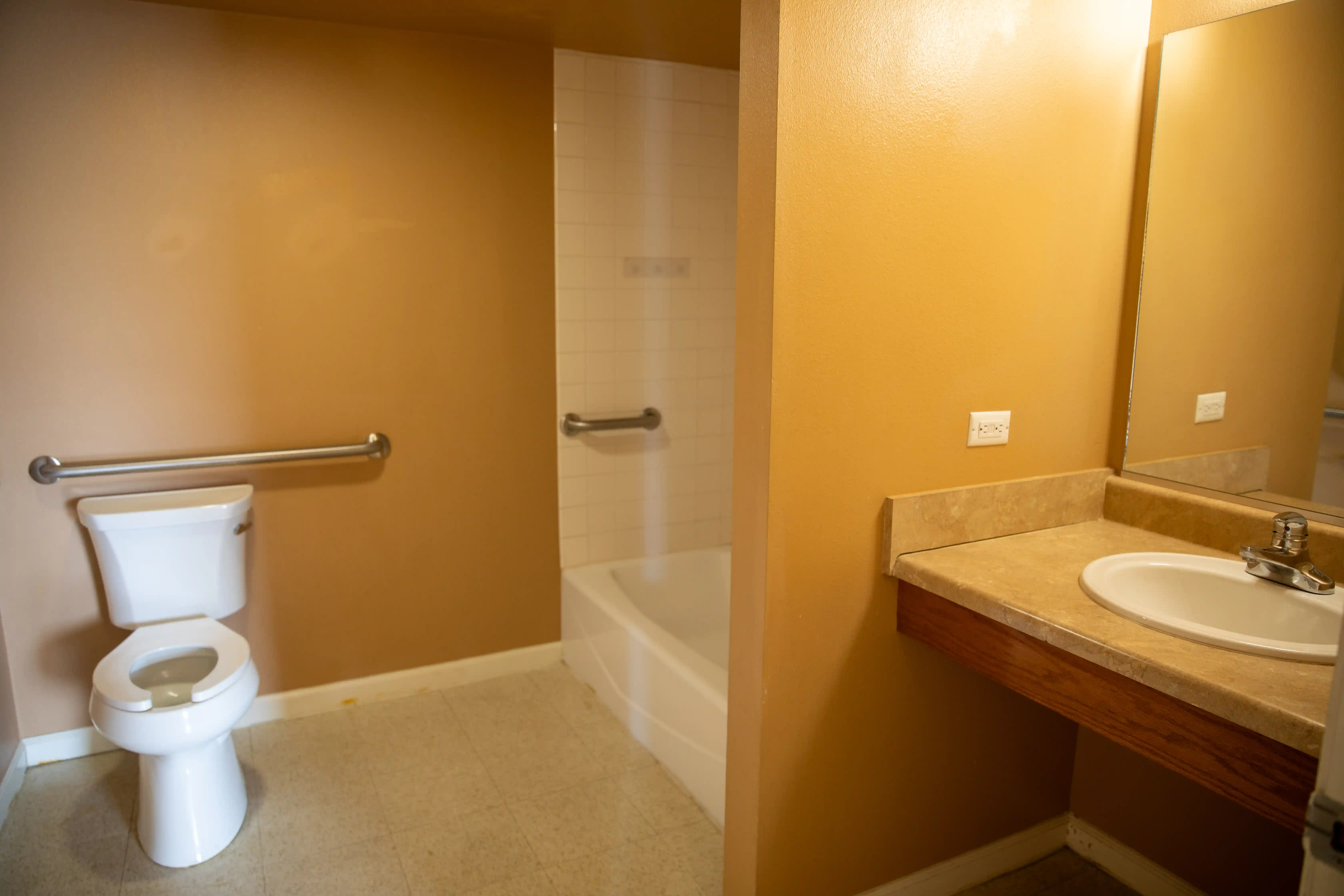 View of a bathroom with tub/shower combo and safety rails.
