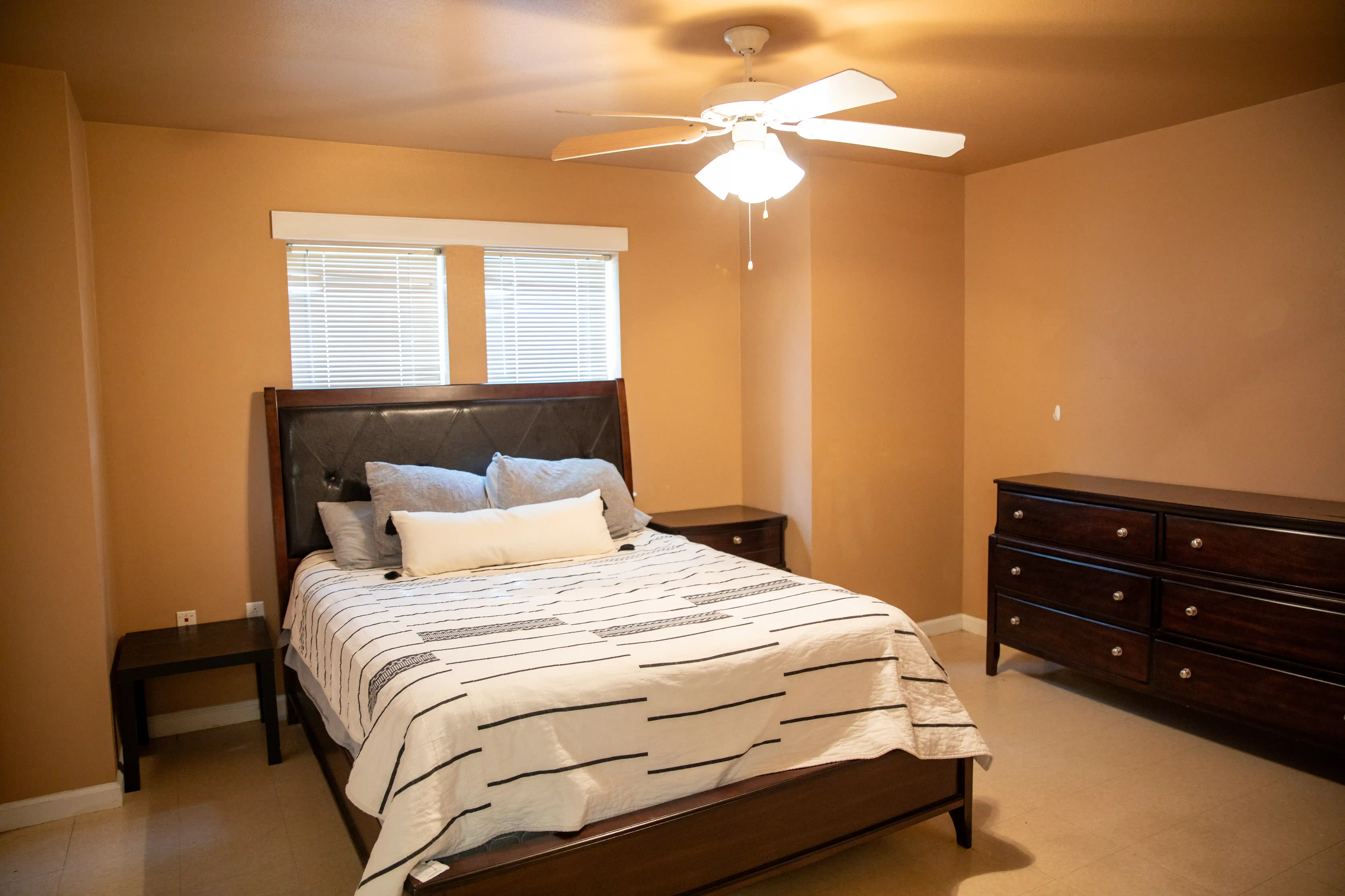 Bedroom with a full-size bed covered in striped bedding, a dresser, and a nightstand near a window with blinds.