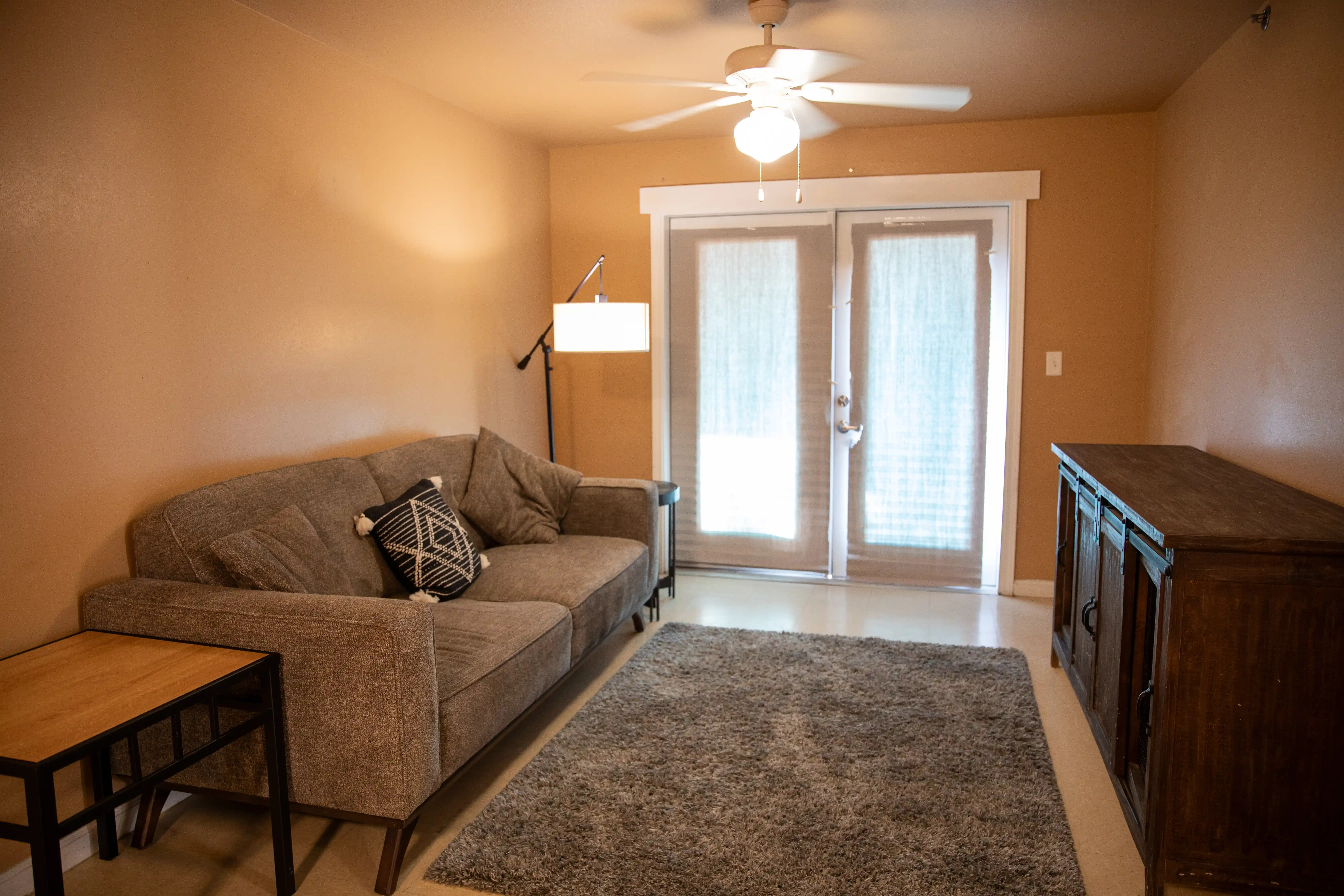 Living room with a sofa, end table, tv stand and lamp, with glass doors leading to the porch.