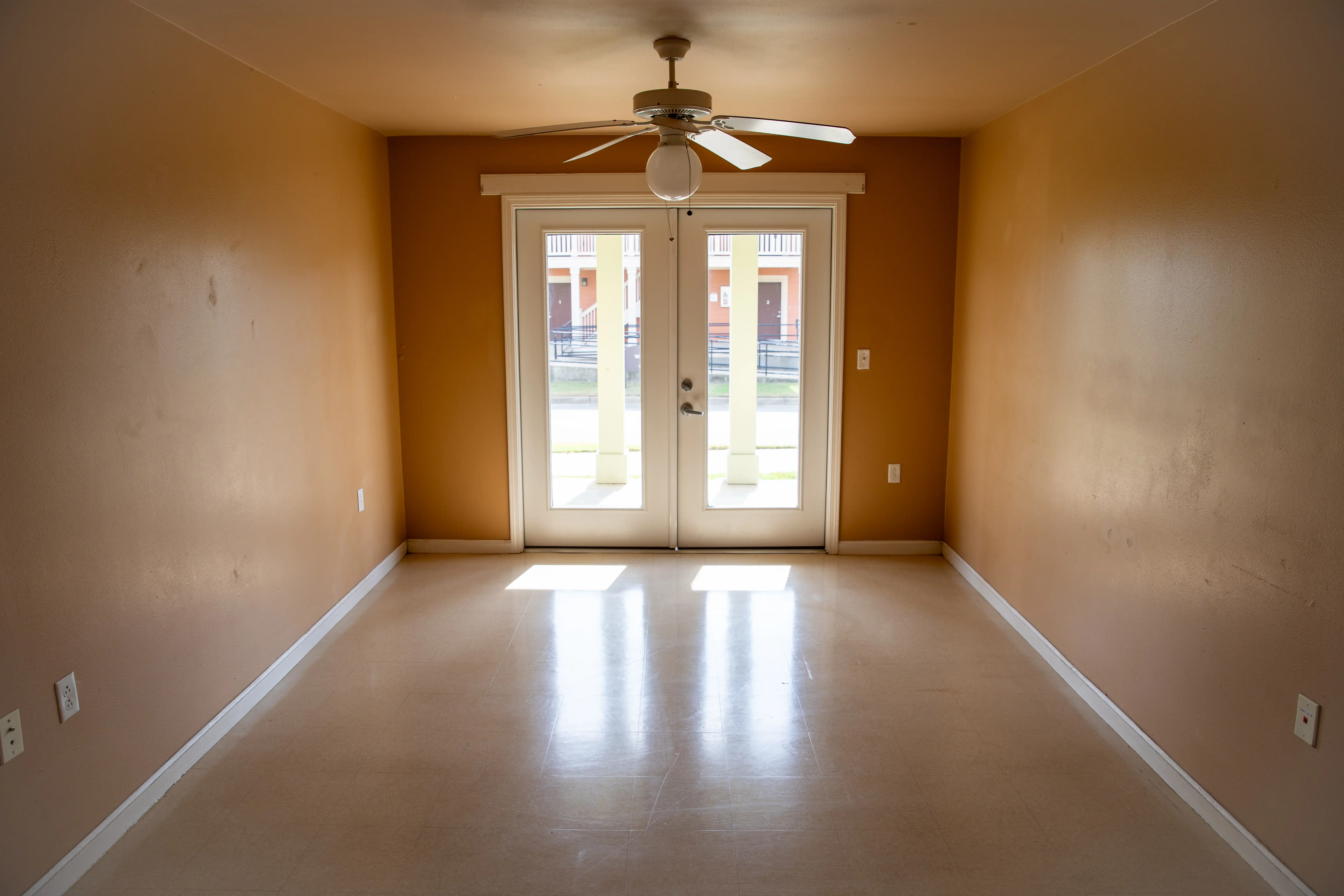 Empty living space with tan walls, ceiling fan, and glass doors opening to a porch.