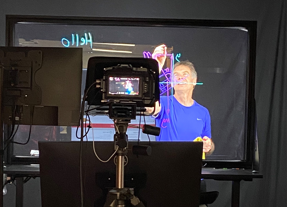 Instructor writing on Lightboard glass in front of studio camera