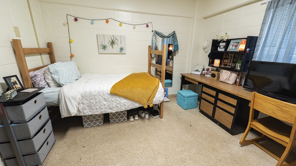 Single bed with white bedding and yellow throw, desk, and dresser in Kays Hall room.