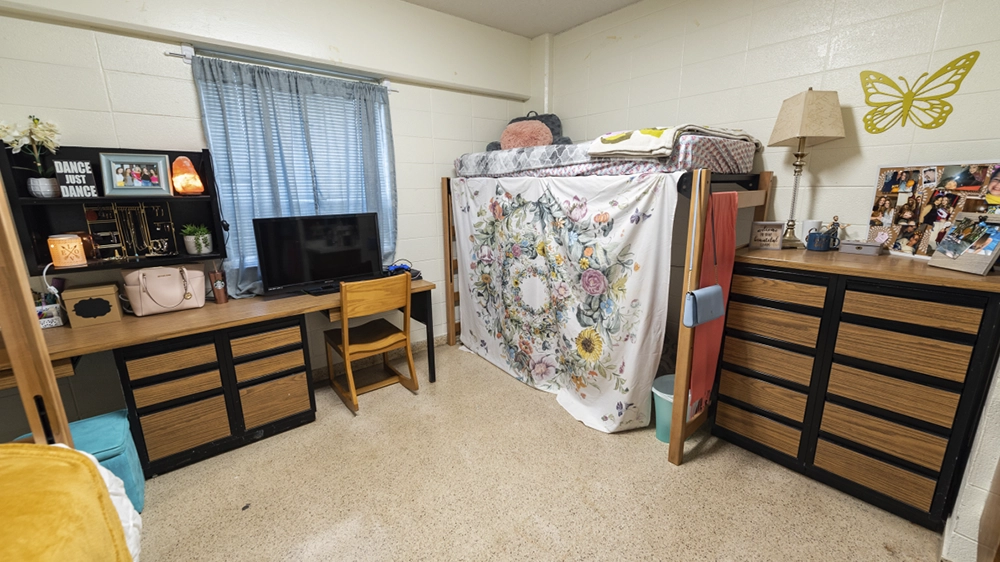 Lofted bed with floral curtain, dresser, and desk in Kays Hall bedroom.