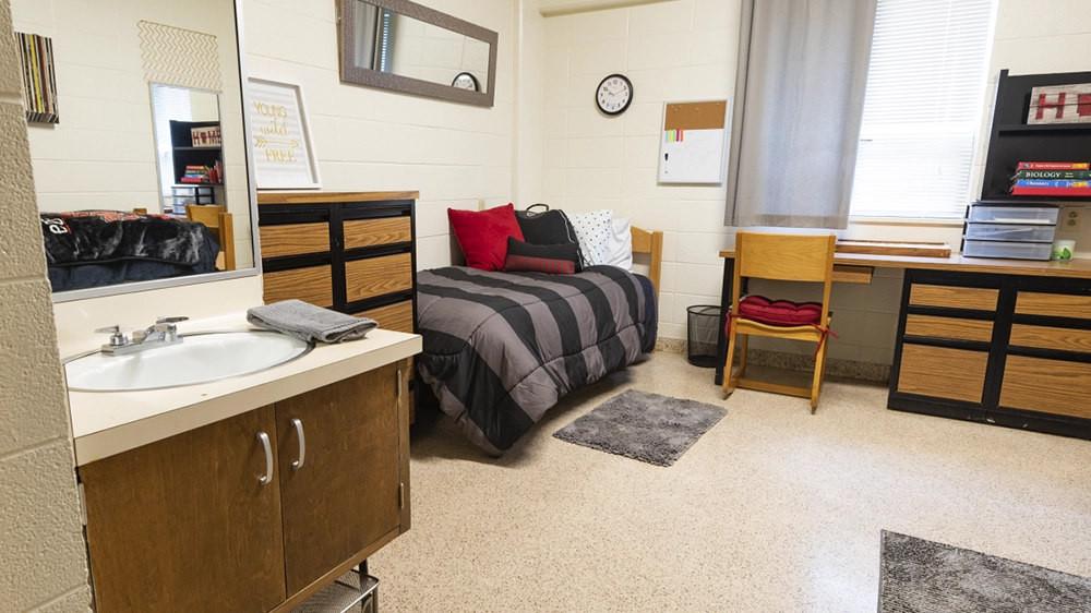 Single bed with black bedding, dresser, and sink with mirror in Kays Hall room.