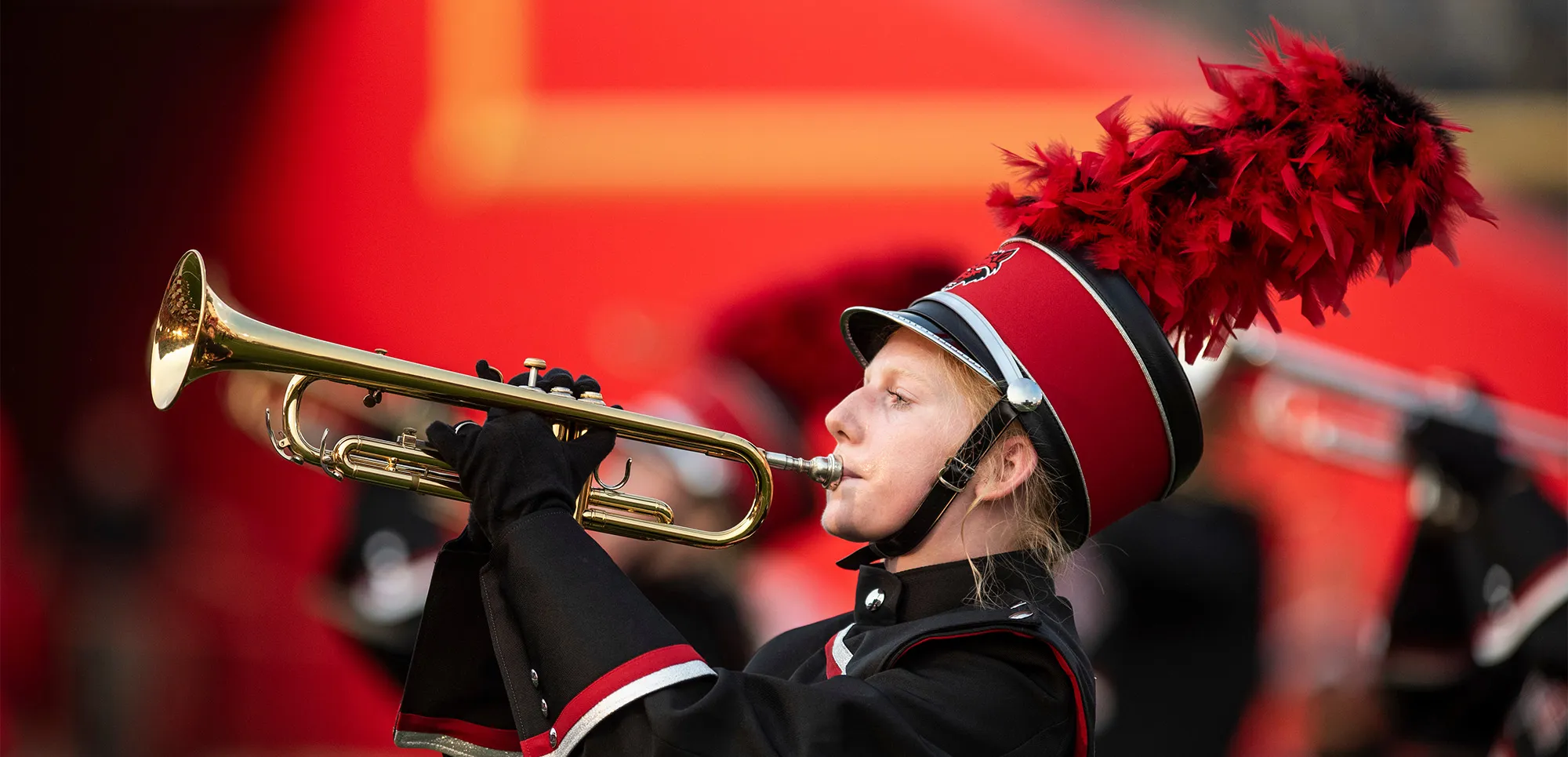 band member playing trumpet with a bright red wall in the background