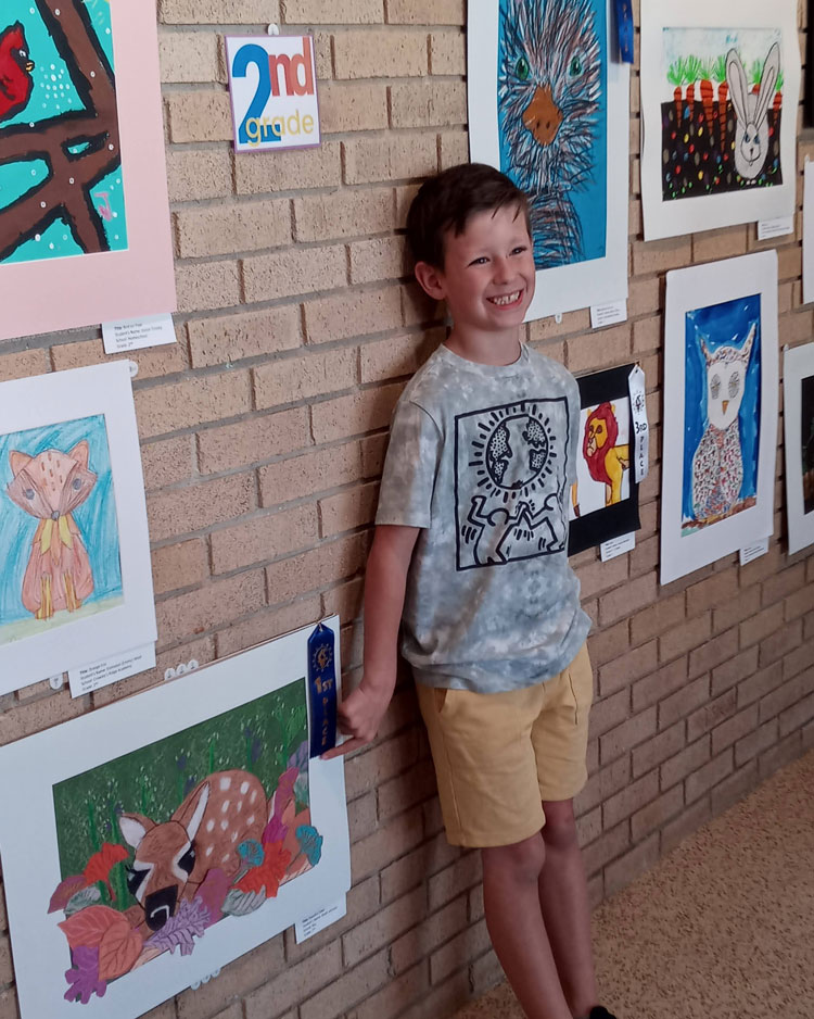 A second grader pointing to his artistic interpretation of a fawn.