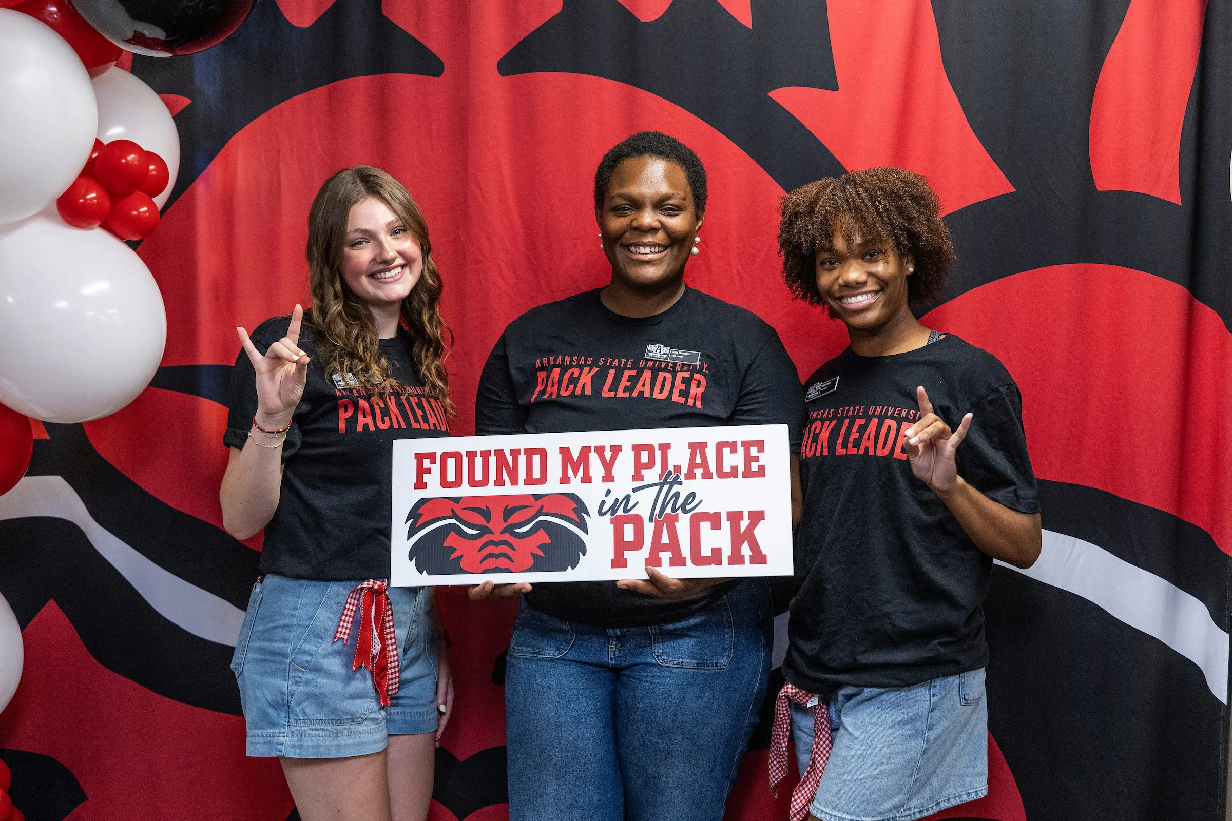Three A-State Pack Leaders smile and pose with a “Found My Place in the Pack” sign.