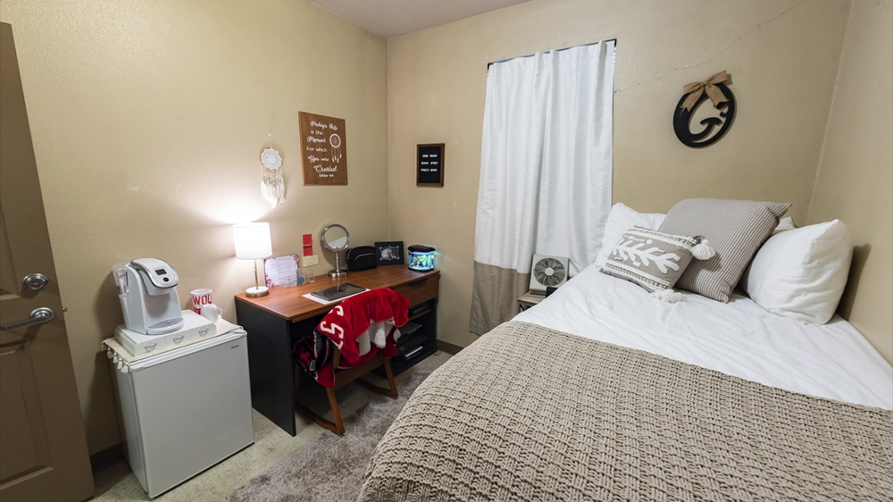 Private bedroom with bed, desk, mini fridge, and wall décor.