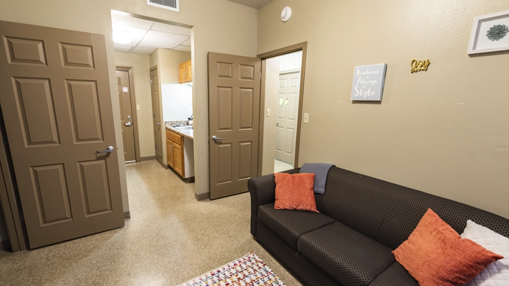 Living room view showing sofa and doorway to kitchenette with cabinets and sink.