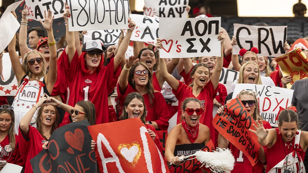 Crowd dressed in red holding handmade signs and cheering at a campus pep rally event.