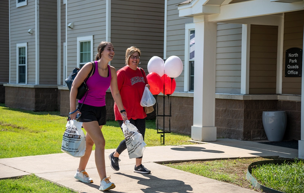 Female Student and Mother Carrying Textbooks past the North Park Quads Office