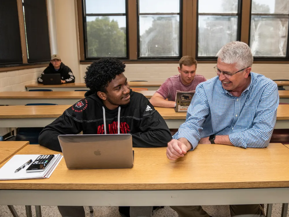 Dr. Powell laughing with a student in class going over work on laptop