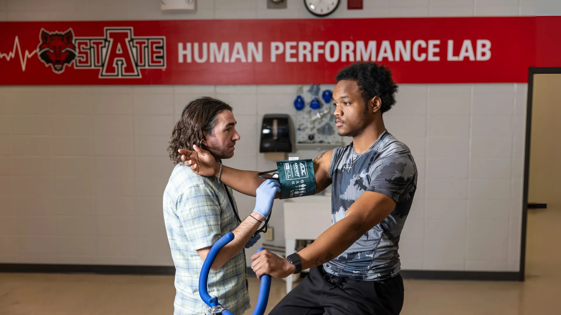 A professor recording a student's heartrate as they exercise.
