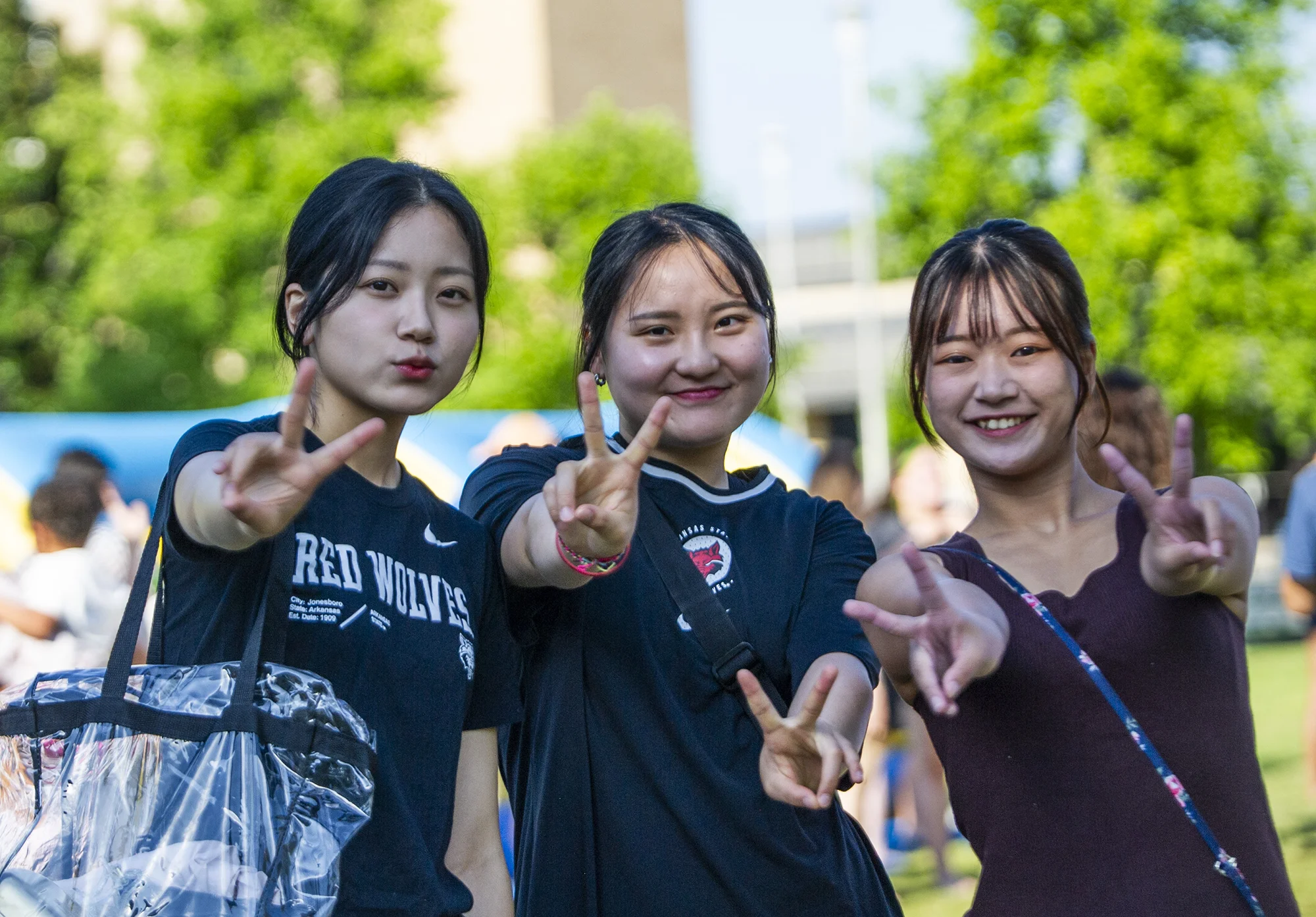 Three students in Red Wolves gear holding up peace signs.