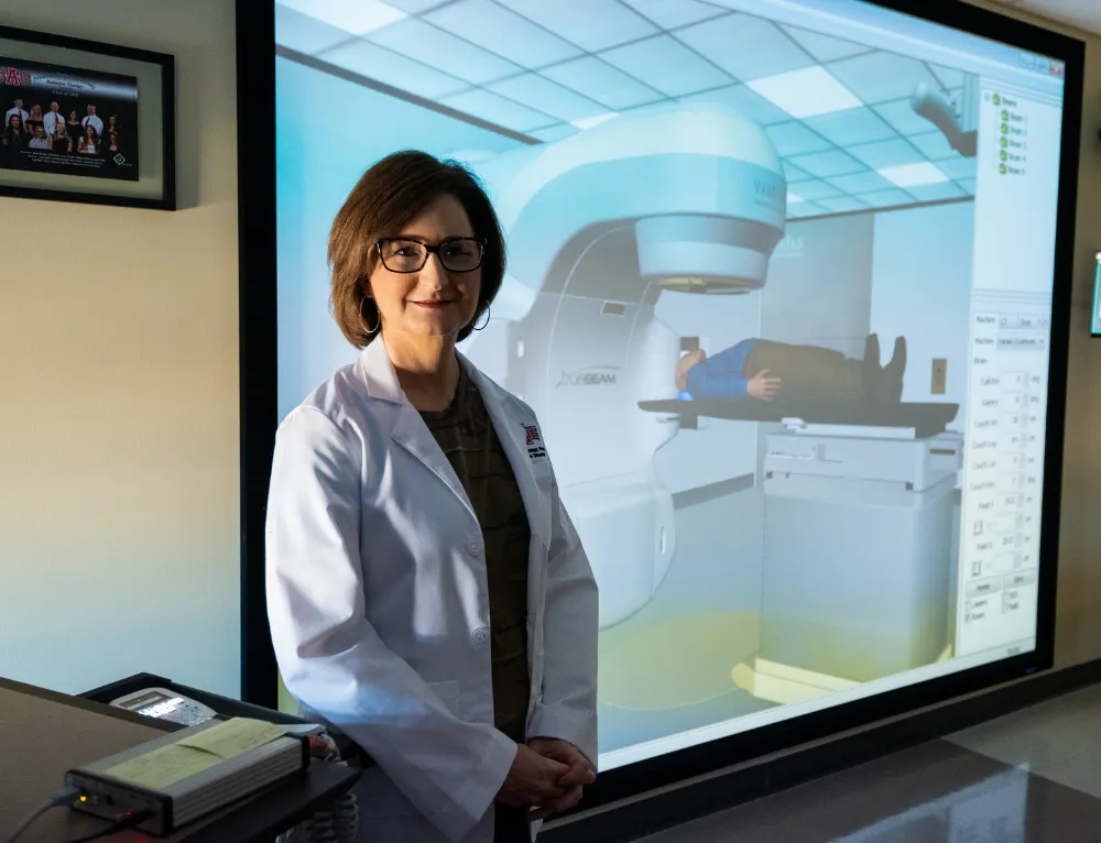 A-State radiology professor standing by virtual reality MRI machinein A-State scrubs