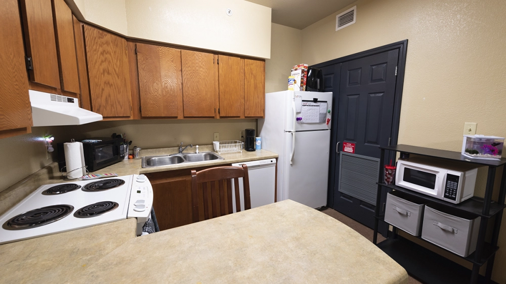 Kitchen in Red Wolf Den apartment featuring electric stove, microwave, refrigerator, dishwasher, wooden cabinets, and bar-style counter seating.