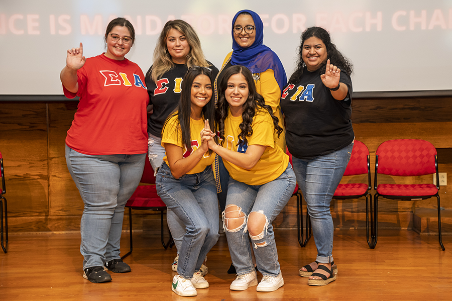Sorority women in greek-letter shirts pose on a stage at a leadership event.