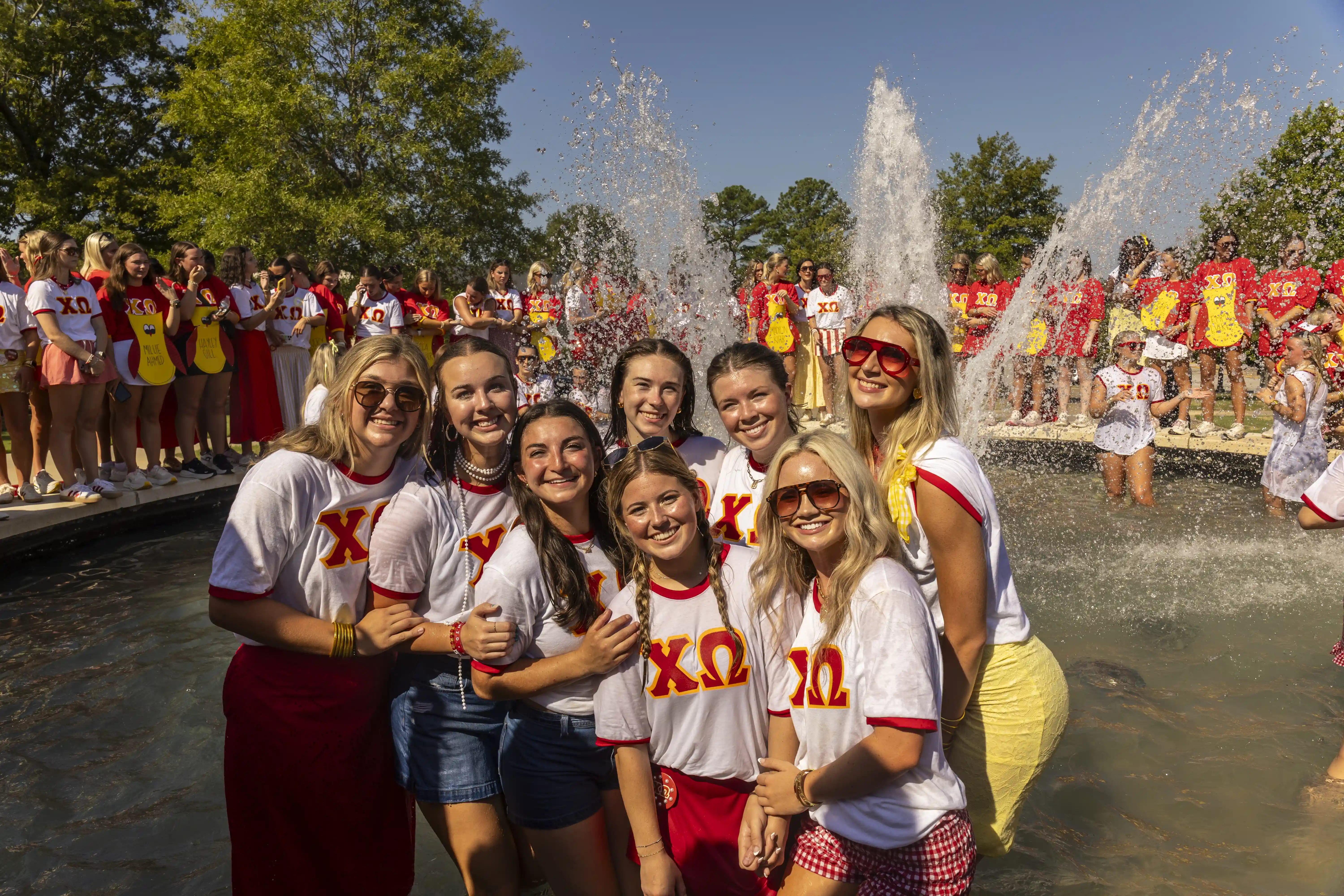 Chi Omega sorority women posing in fountain on Sorority Bid Day with sisters in the background.