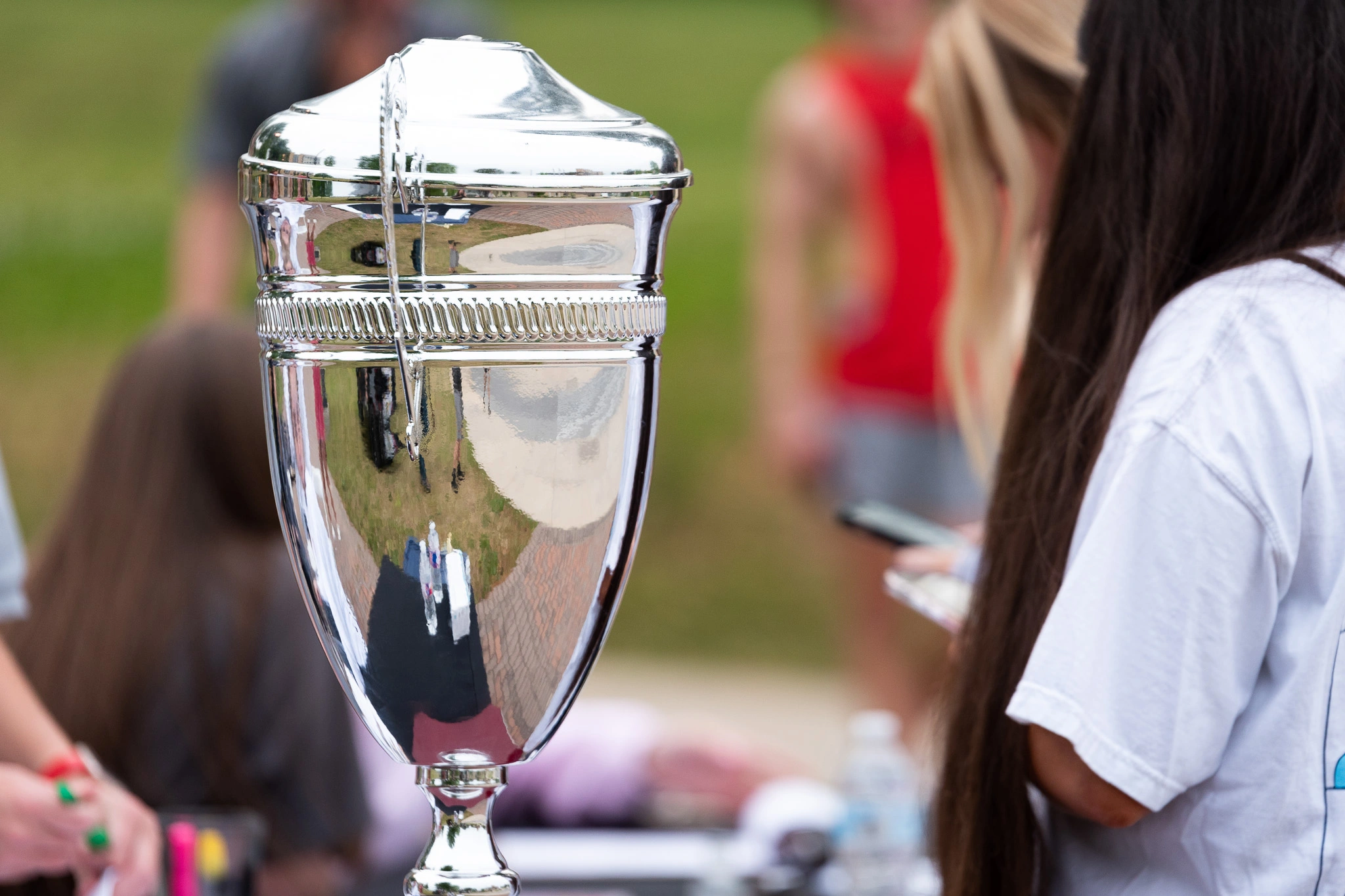 A large silver trophy sits on a table during an Arkansas State University event, reflecting students gathered nearby as they participate in campus activities.